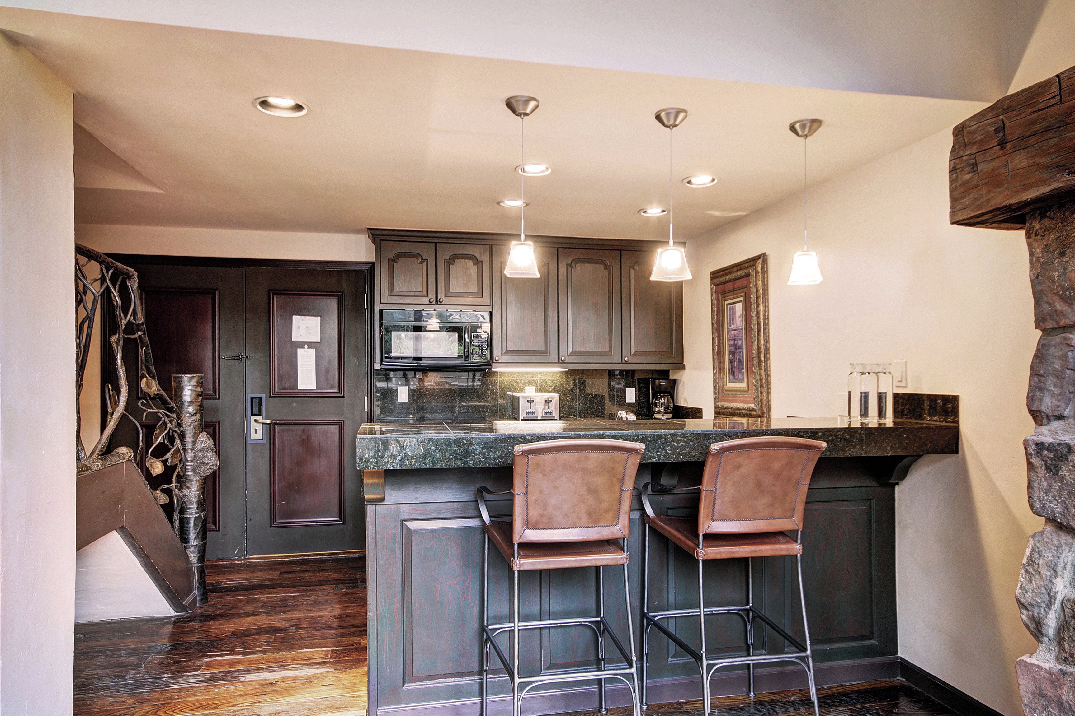 A kitchen with dark wooden cabinets, a granite countertop, and two bar stools.