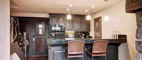A kitchen with dark wooden cabinets, a granite countertop, and two bar stools.