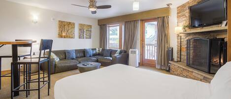 A hotel room with a large bed, a sofa, a dining table with chairs, a fireplace, and a TV mounted on the wall.