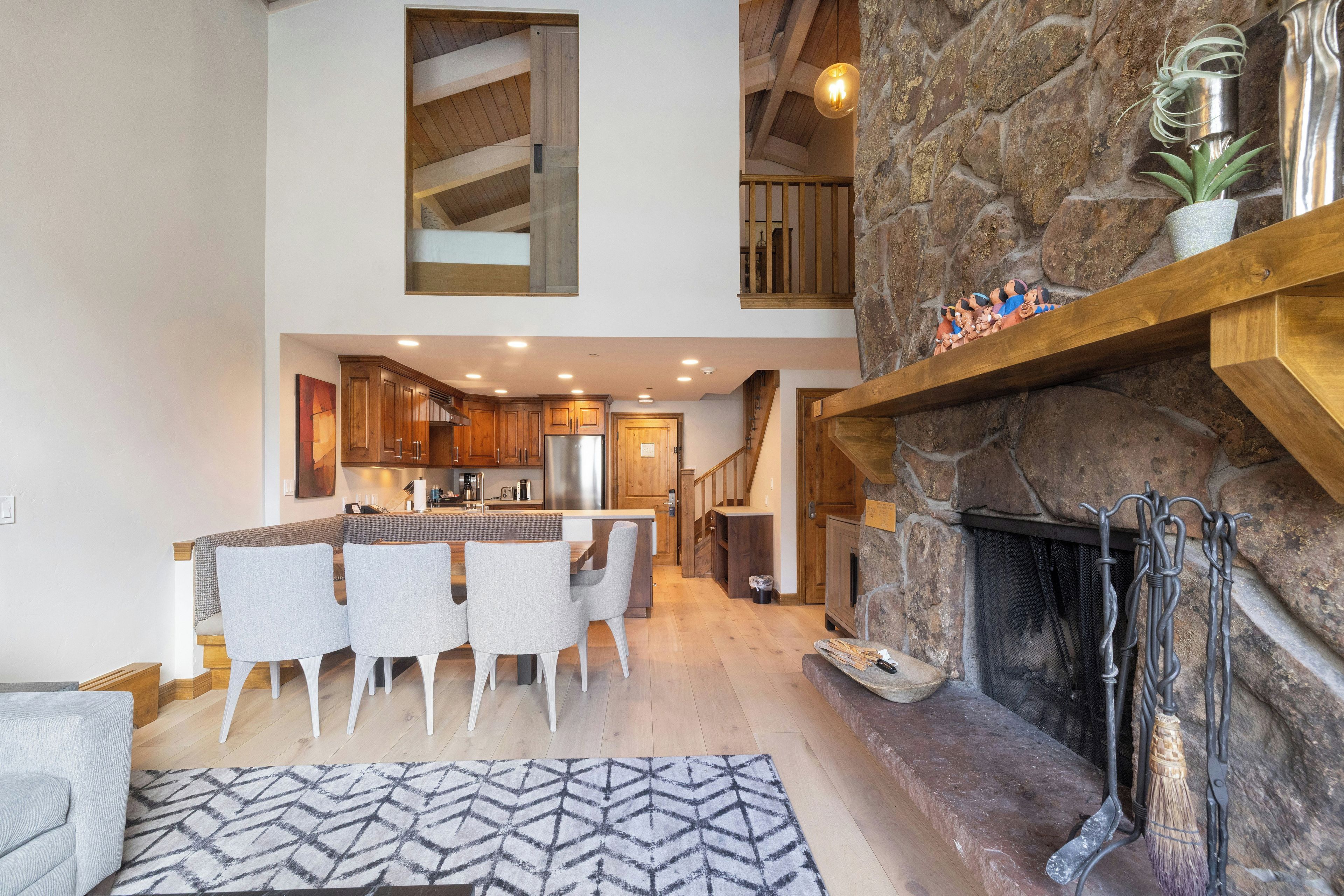 A spacious kitchen with wooden cabinets, a dining area with chairs, a fireplace, and a stone wall.