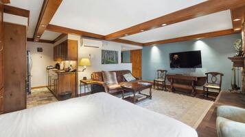 A hotel room with a large bed, a sitting area with a sofa and chairs, a television, and a kitchenette.