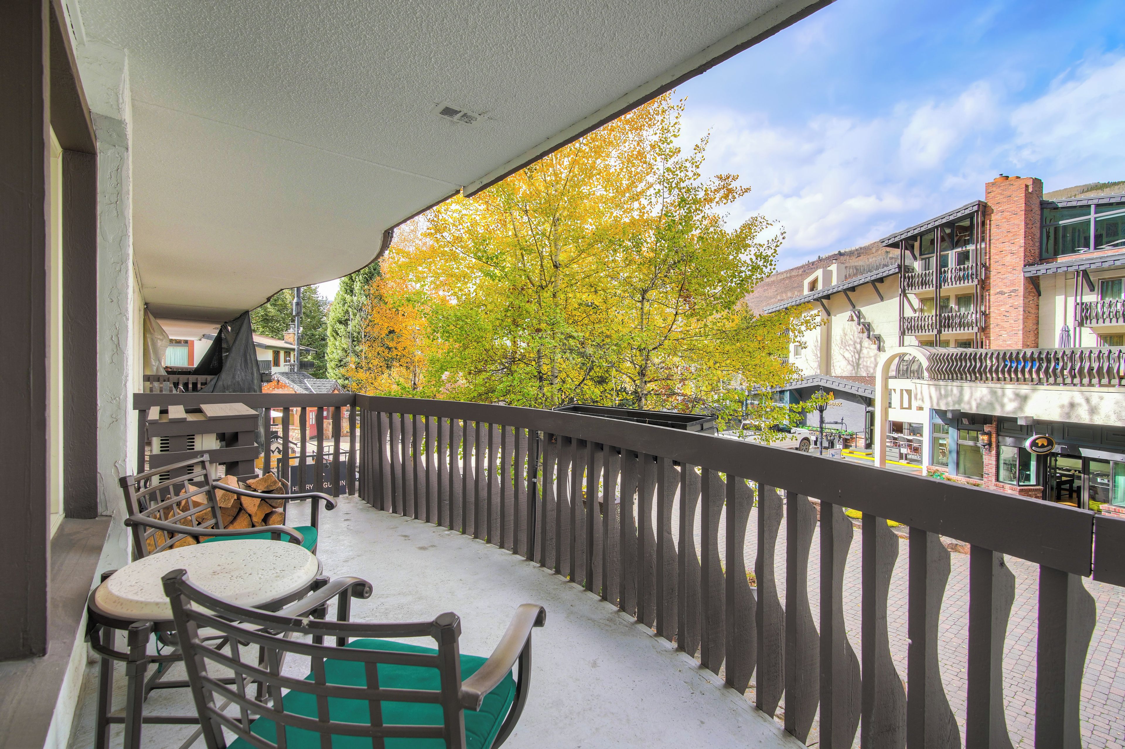 A balcony with a view of autumn trees, a brick building, and a restaurant.