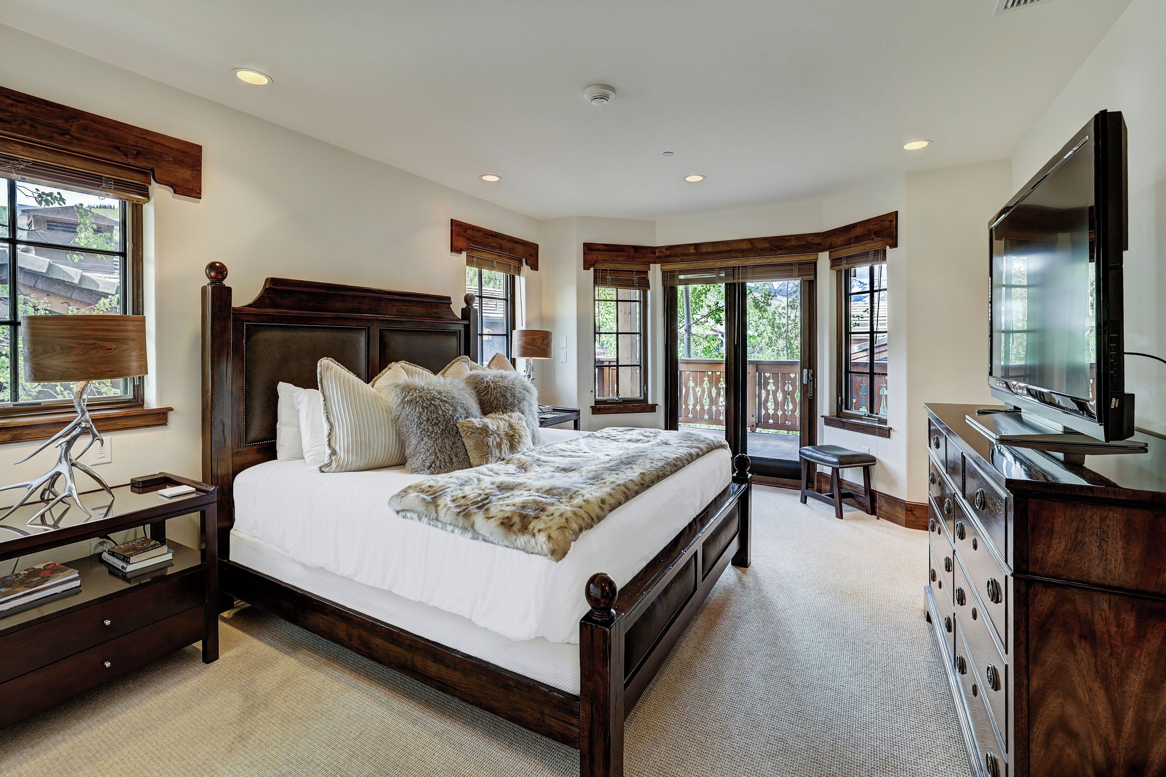A bedroom with a large bed, a dresser, a TV, and a window with a view.
