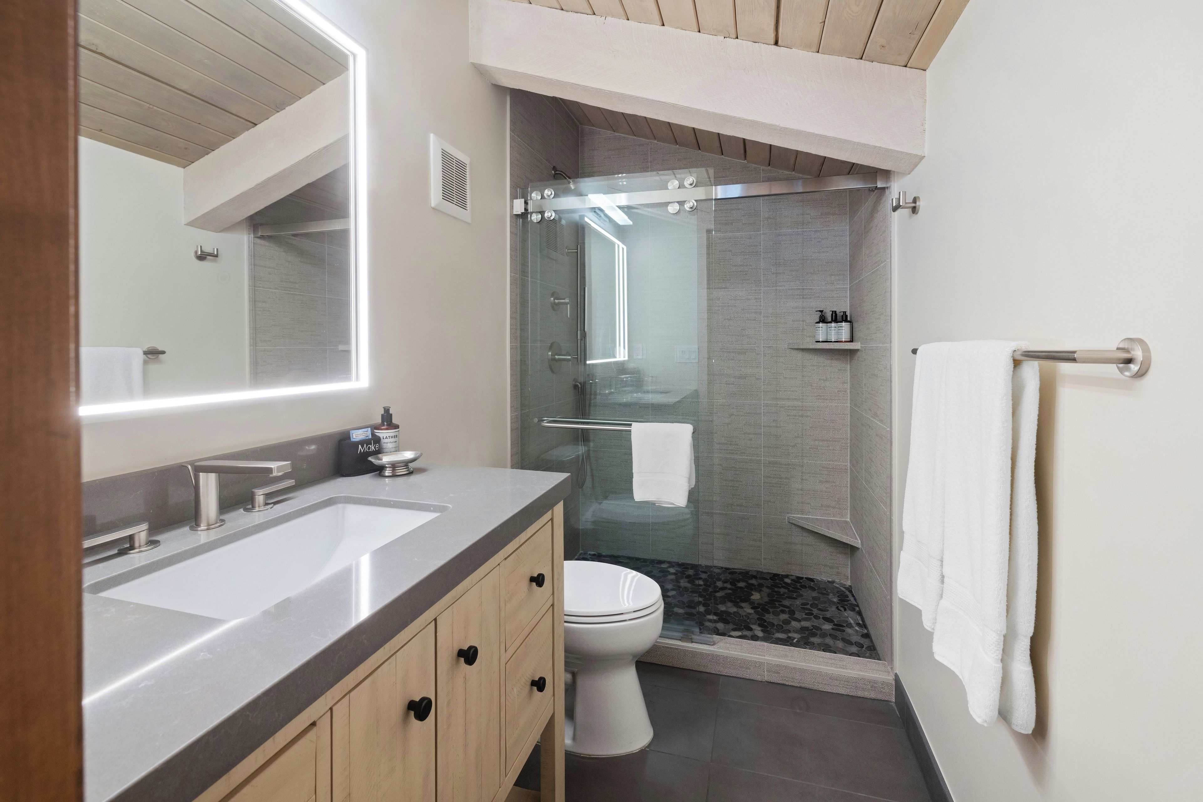 A modern bathroom with a double sink, toilet, and glass-enclosed shower.