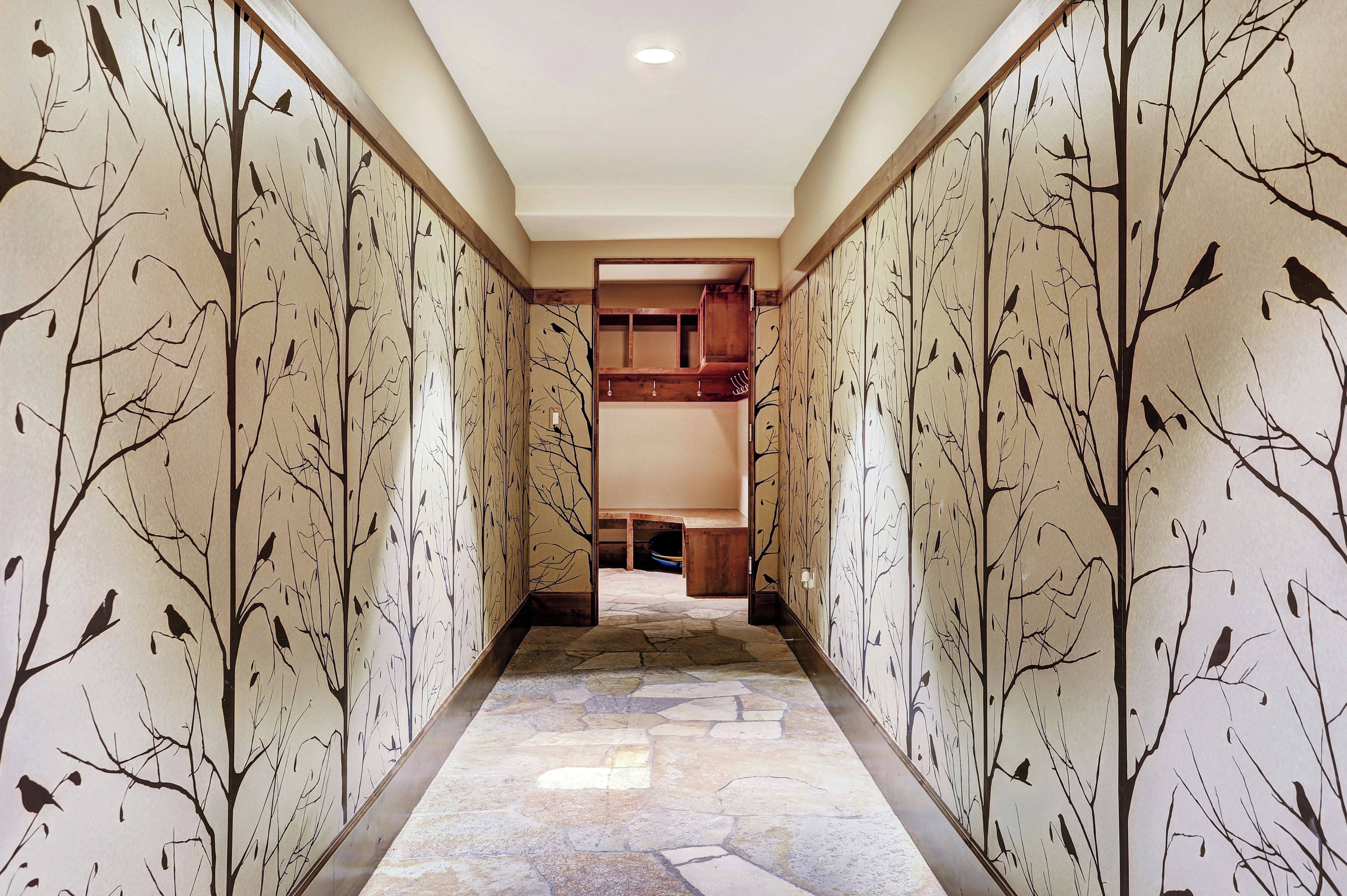 A hallway with patterned walls and a stone floor, leading to a room with a wooden bench and a mirror.