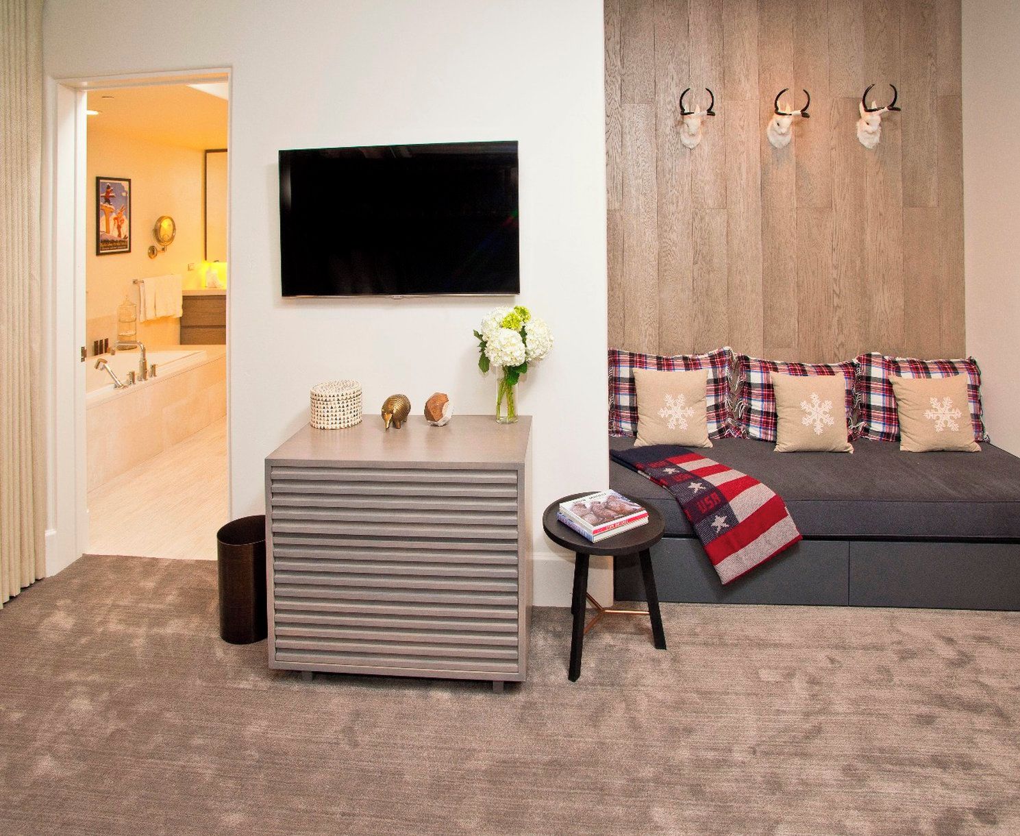 Ein modernes Wohnzimmer mit grauem Sofa, einem flachbildfernseher an der Wand, einem kleinen Tisch mit Dekorationsgegenständen und einer Bank.