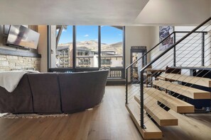A modern living room with a large window, a sofa, a flat-screen TV, and a staircase. - The Lodge at Vail, a RockResort by Vail Resorts (Vail)