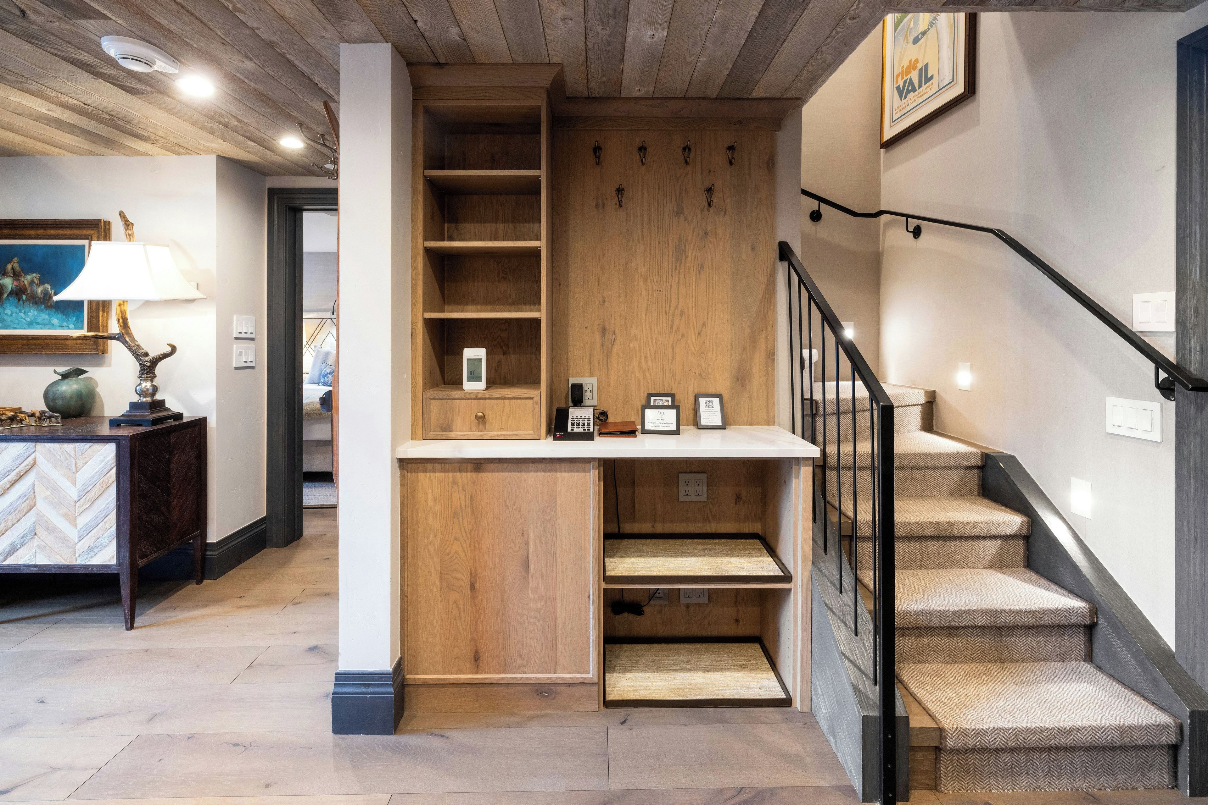 A wooden staircase with a black railing, a wooden bench with a lamp, and a wall-mounted telephone.