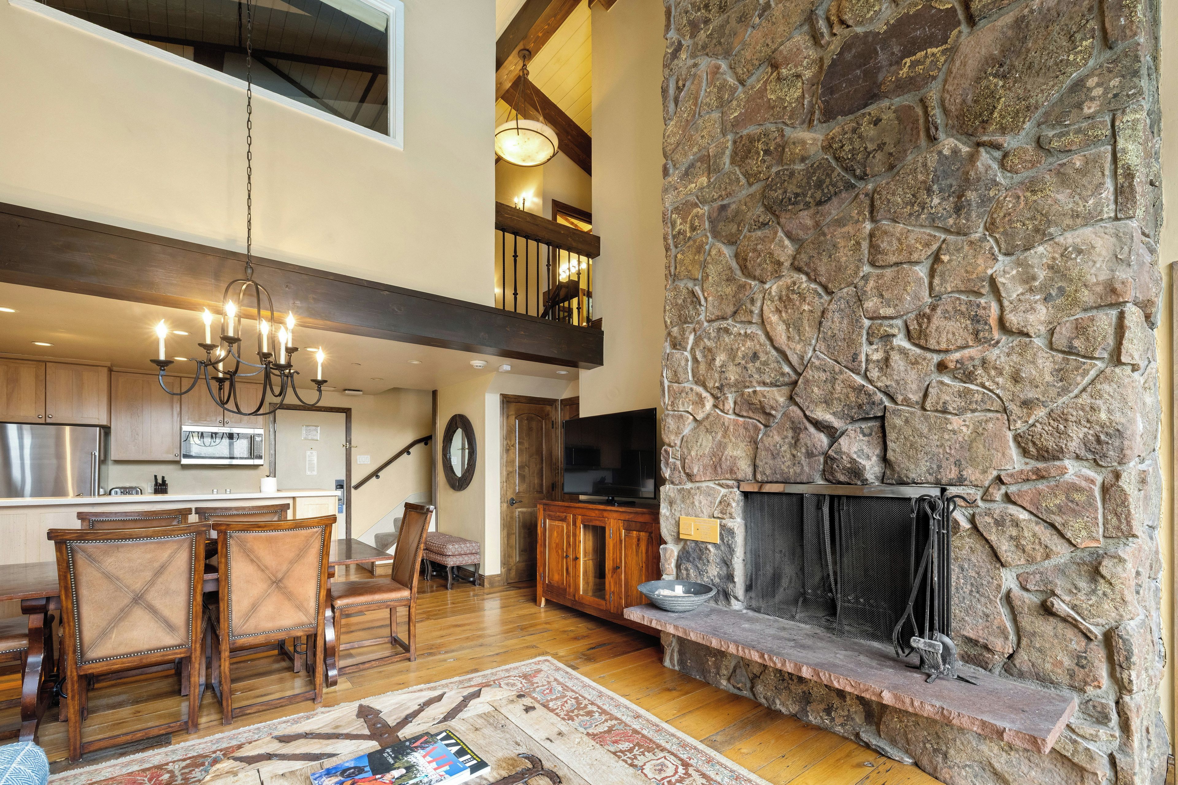 A spacious living area with a stone fireplace, wooden furniture, and a modern kitchen in the background.