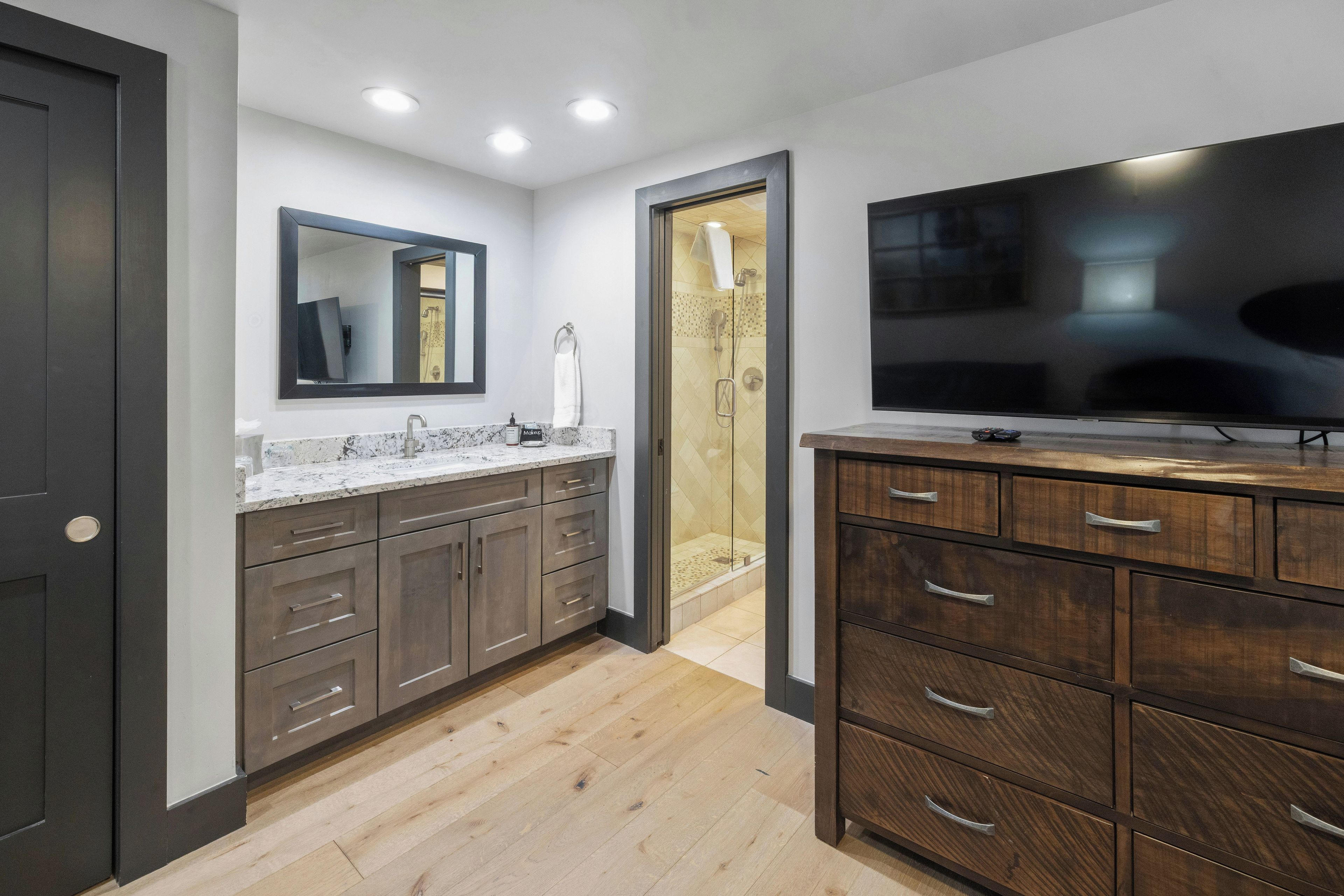 A modern bathroom with a large mirror, a vanity with a TV, and a shower area.