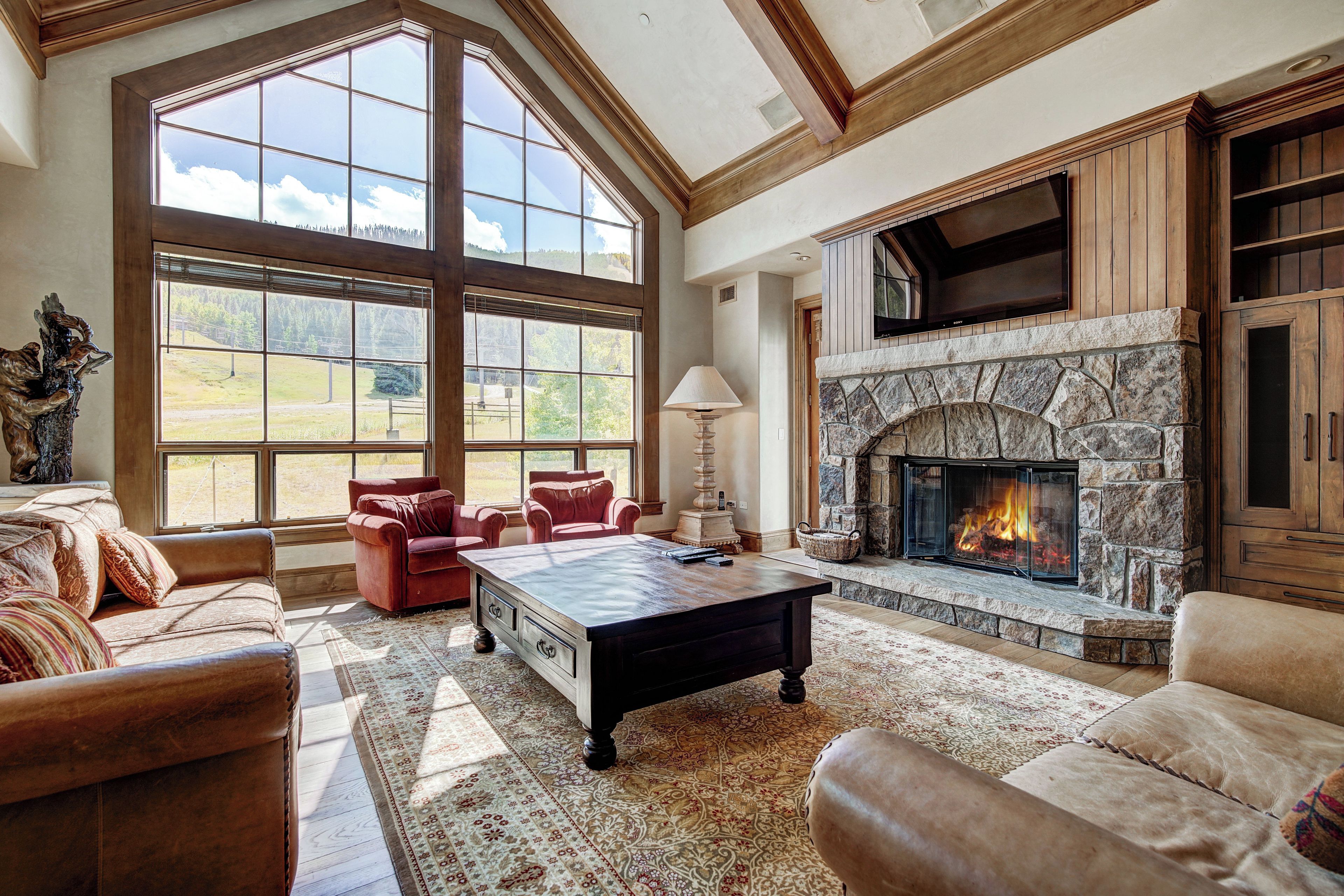 A spacious living room with a stone fireplace, large windows, leather sofas, and a coffee table.