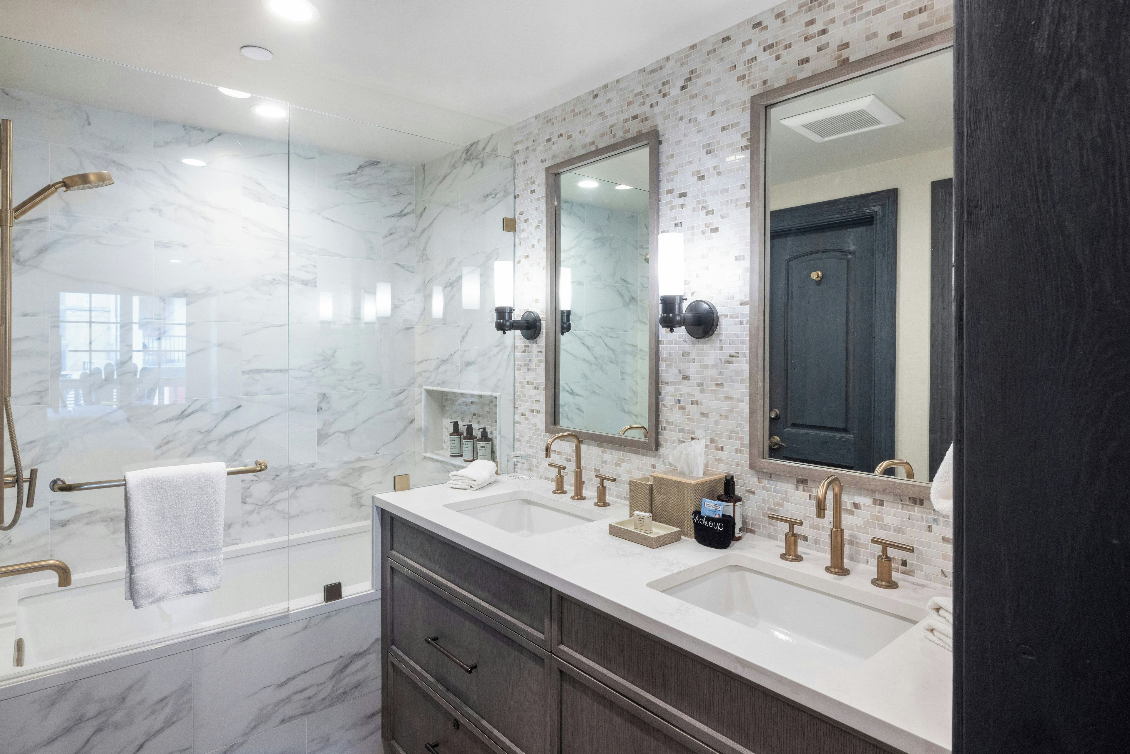 A modern bathroom with a large mirror, two sinks, a bathtub, and a vanity with drawers.