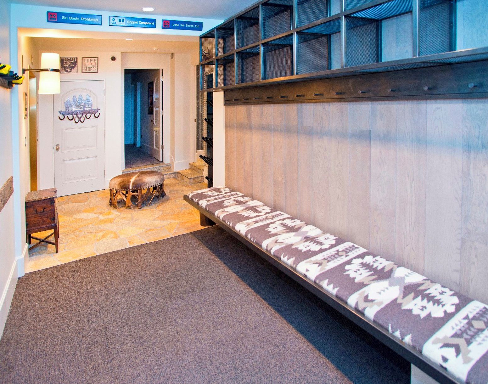 A hotel hallway with a bench, a wooden stool, and a door with a sign.