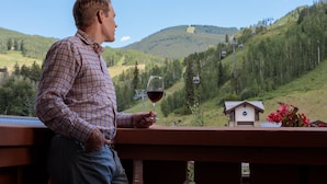 A man standing on a balcony overlooking a mountainous landscape with a small cabin and a ski lift in the background. - The Lodge at Vail, a RockResort by Vail Resorts (Vail)