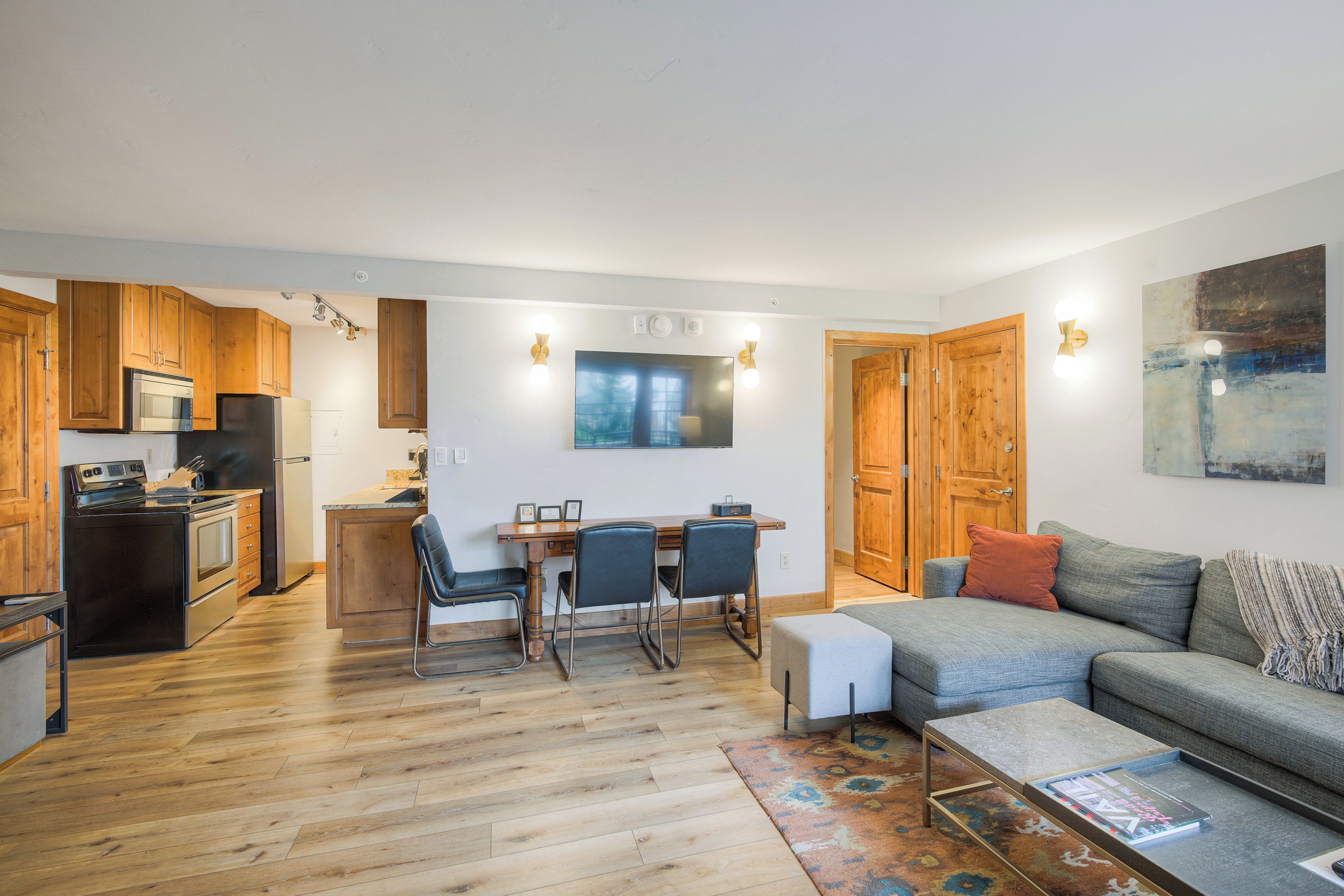 Una cocina moderna con armarios de madera, un comedor con mesa y sillas, un sofá gris y una mesa de centro.