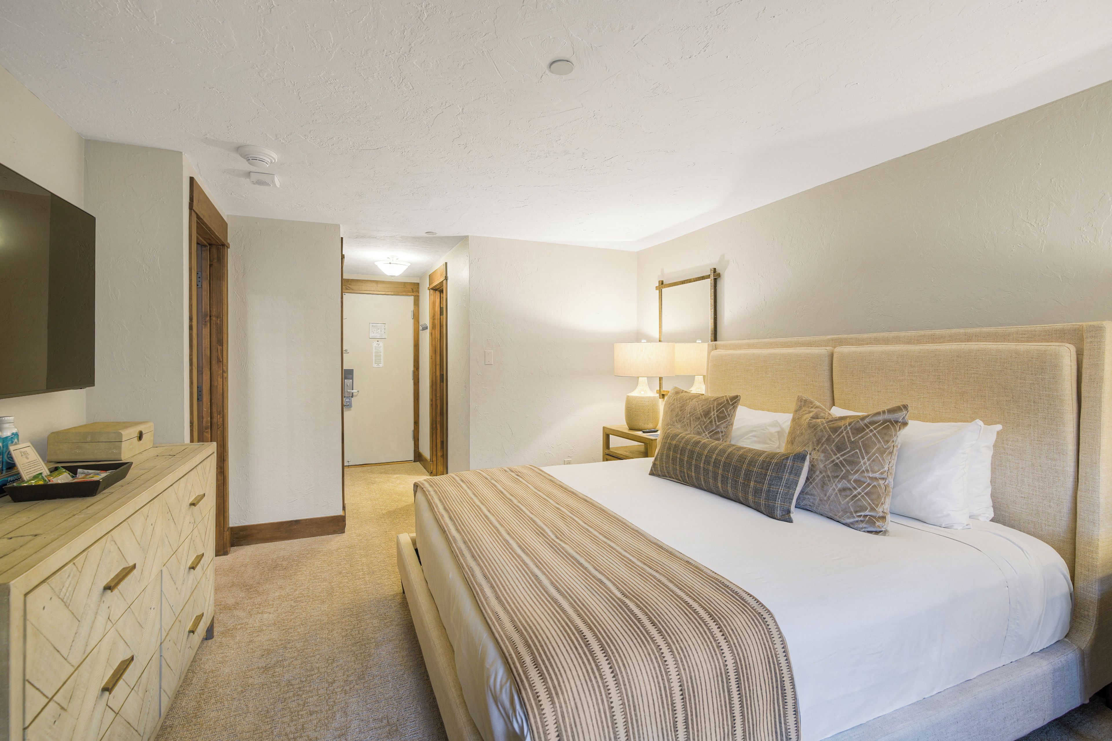 A hotel room with a large bed, a dresser, a television, and a door leading to another room.
