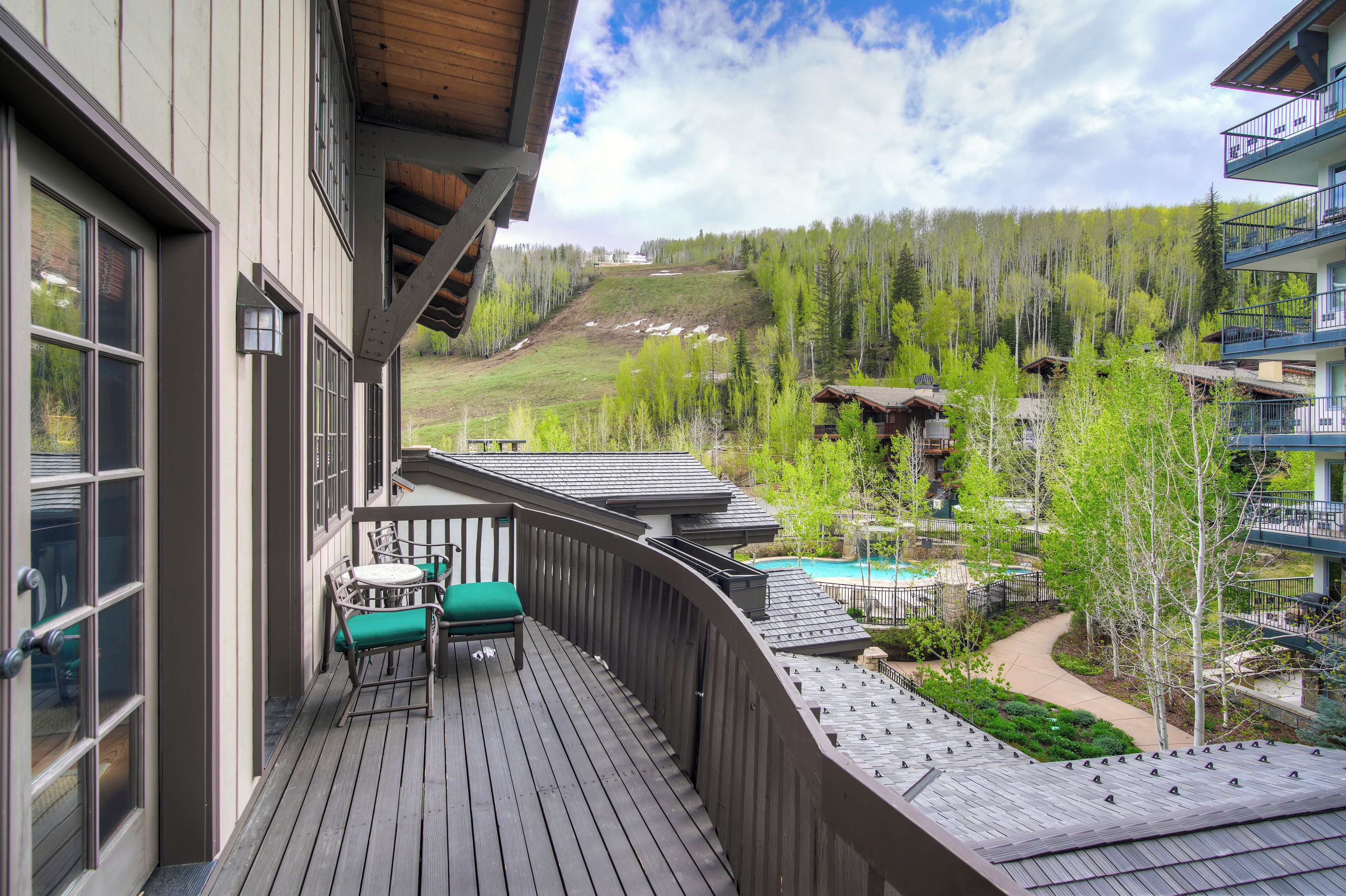 A wooden deck with outdoor seating, overlooking a mountainous landscape and a pool area.