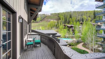 A wooden deck with outdoor seating, overlooking a mountainous landscape and a pool area.