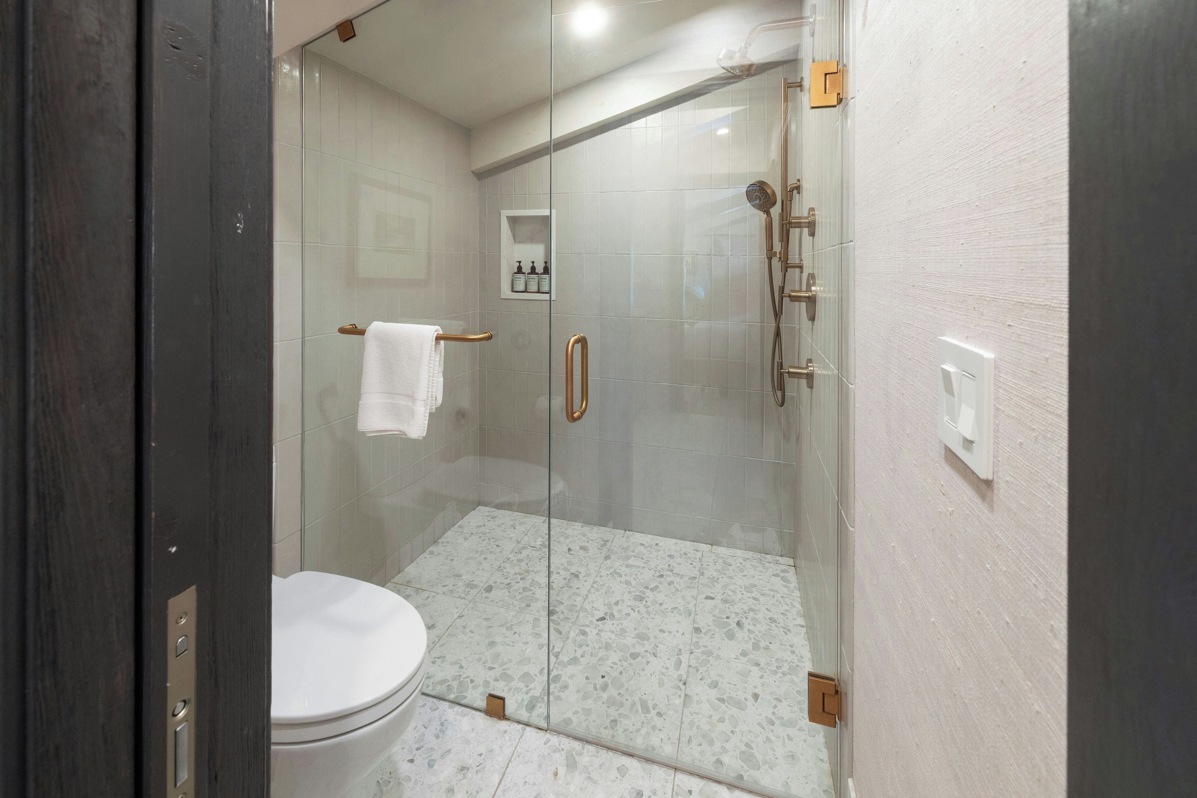 A glass-enclosed shower stall with a white toilet and a towel rack.