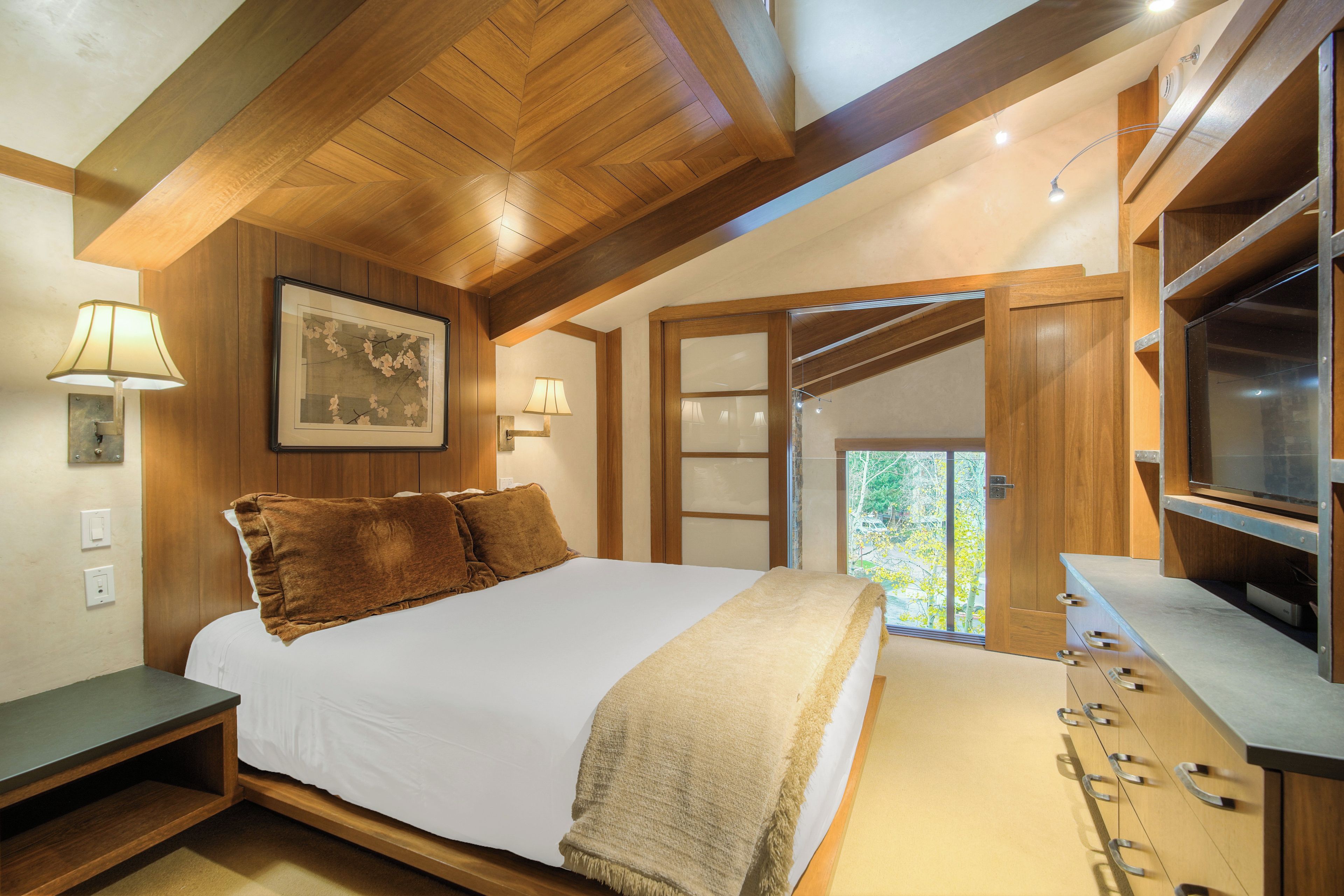 Een slaapkamer met een groot bed, houten plafond en een televisie op een kast.