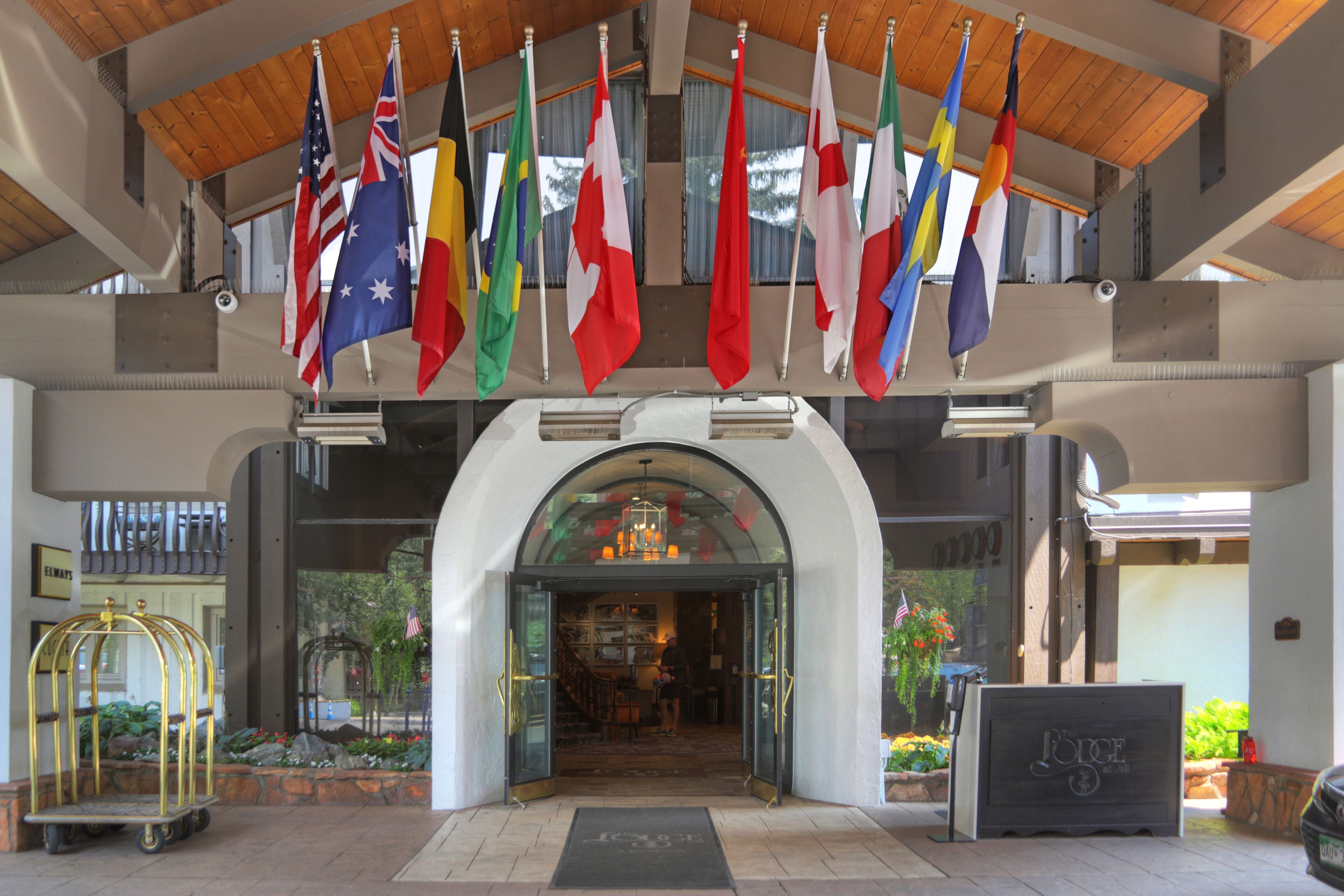 A hotel entrance with multiple national flags, a reception desk, and a bellhop cart.