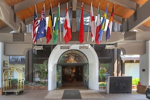 Entrada de hotel con varias banderas nacionales, una recepción y un carrito de botones.