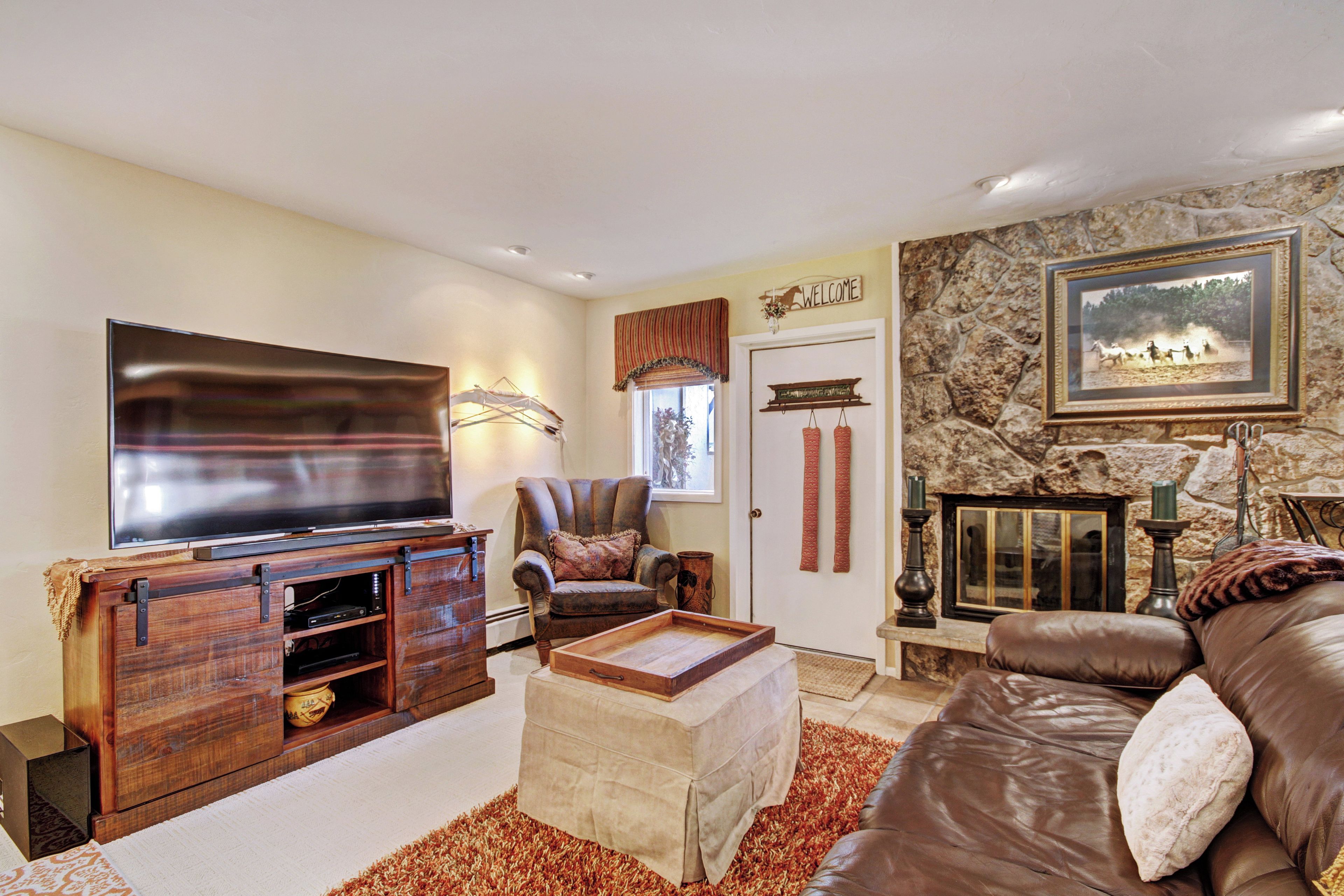A living room with a flat-screen TV, leather sofa, and a stone wall.
