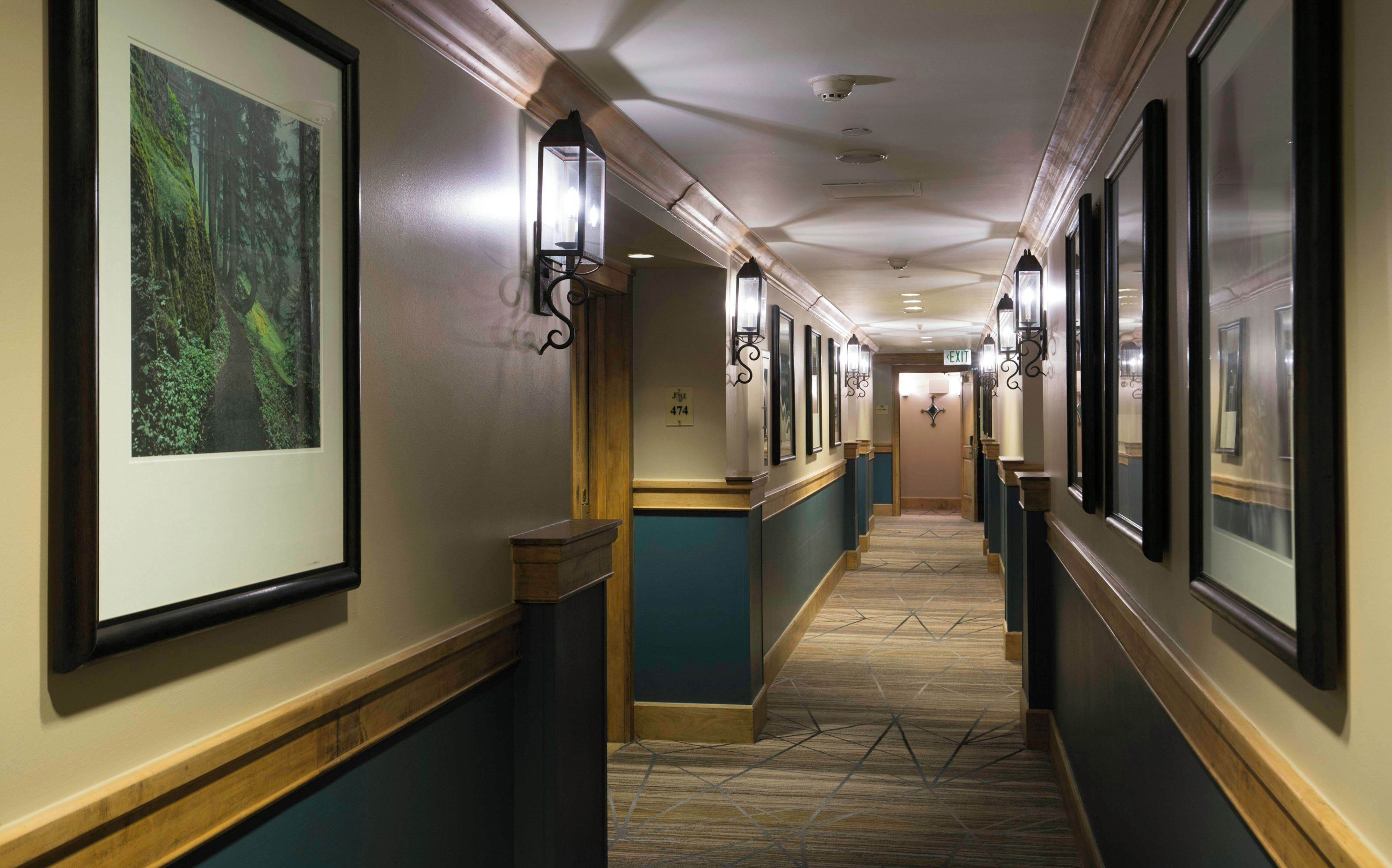 A hotel corridor with framed artwork, wall sconces, and a patterned carpet.