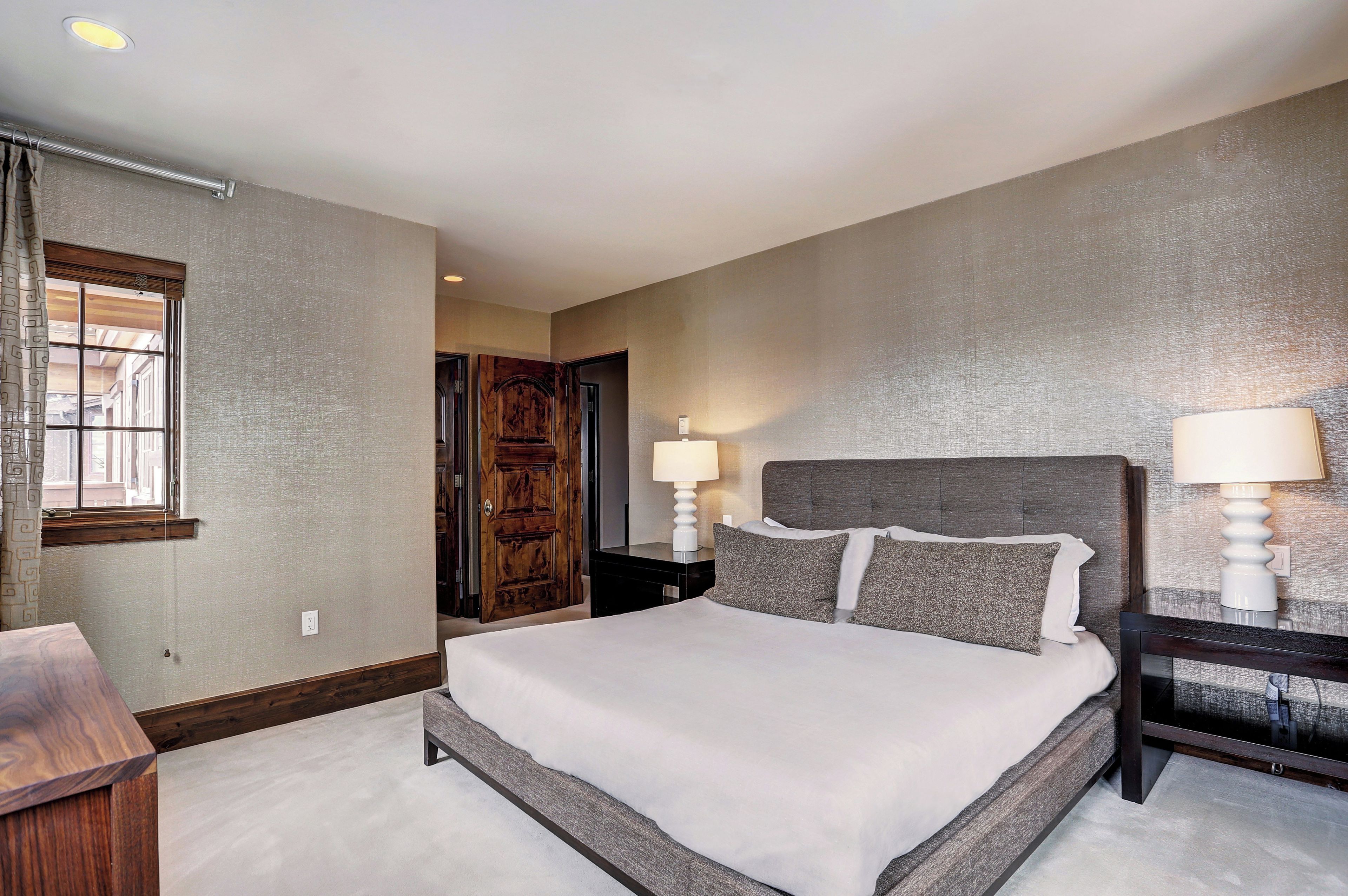 A hotel room with a large bed, two bedside tables with lamps, a wooden door, and a window with curtains.