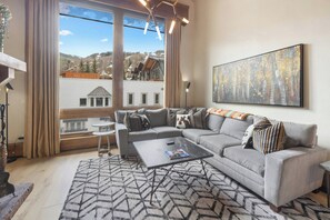 A modern living room with a large window, a gray sofa, a coffee table, and a patterned rug.
