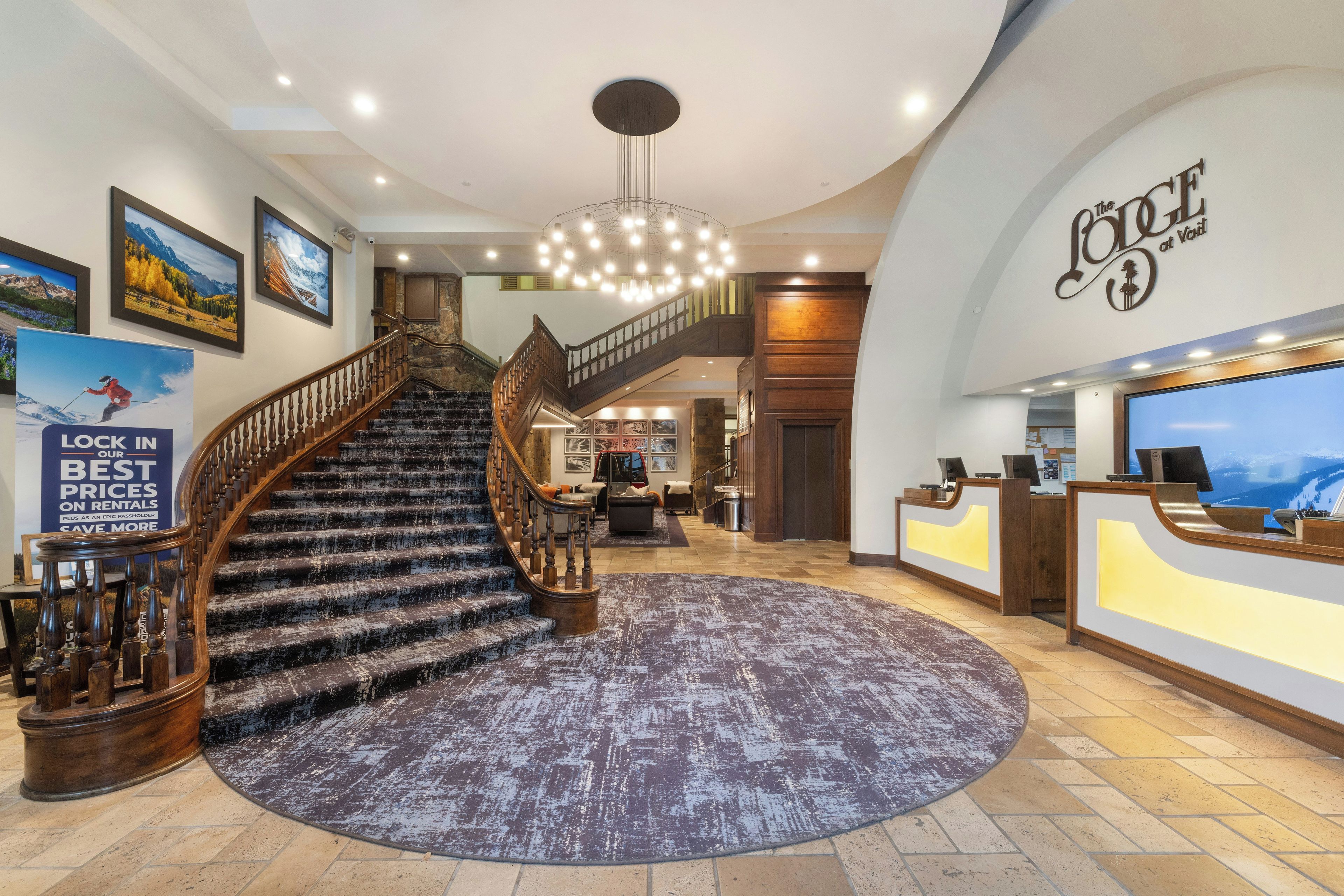 A hotel lobby with a grand staircase, a reception desk, and a large chandelier.