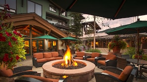 A circular stone fire pit surrounded by wicker chairs and tables, with green umbrellas providing shade. - The Lodge at Vail, a RockResort by Vail Resorts (Vail)