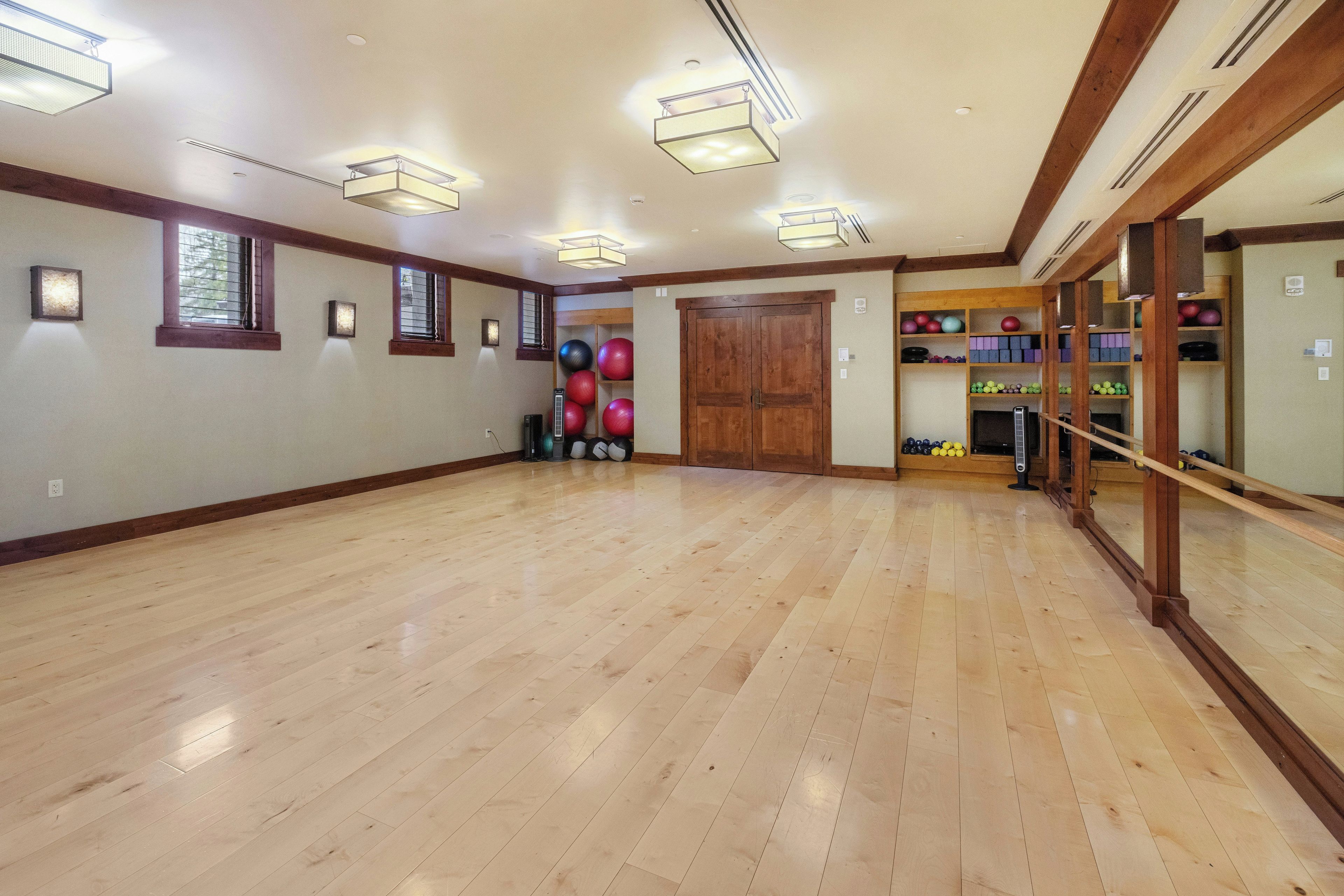 A spacious room with wooden flooring, a large mirror, and exercise equipment.