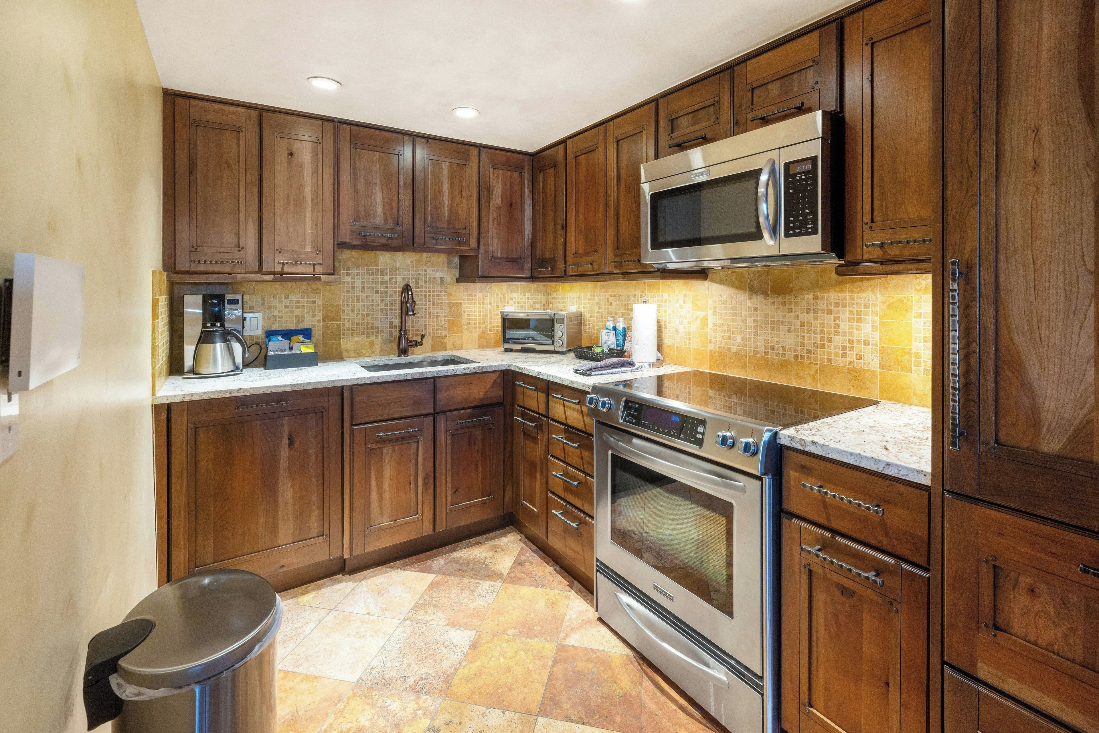 Cocina con armarios de madera, microondas de acero inoxidable, horno empotrado y encimera de granito.