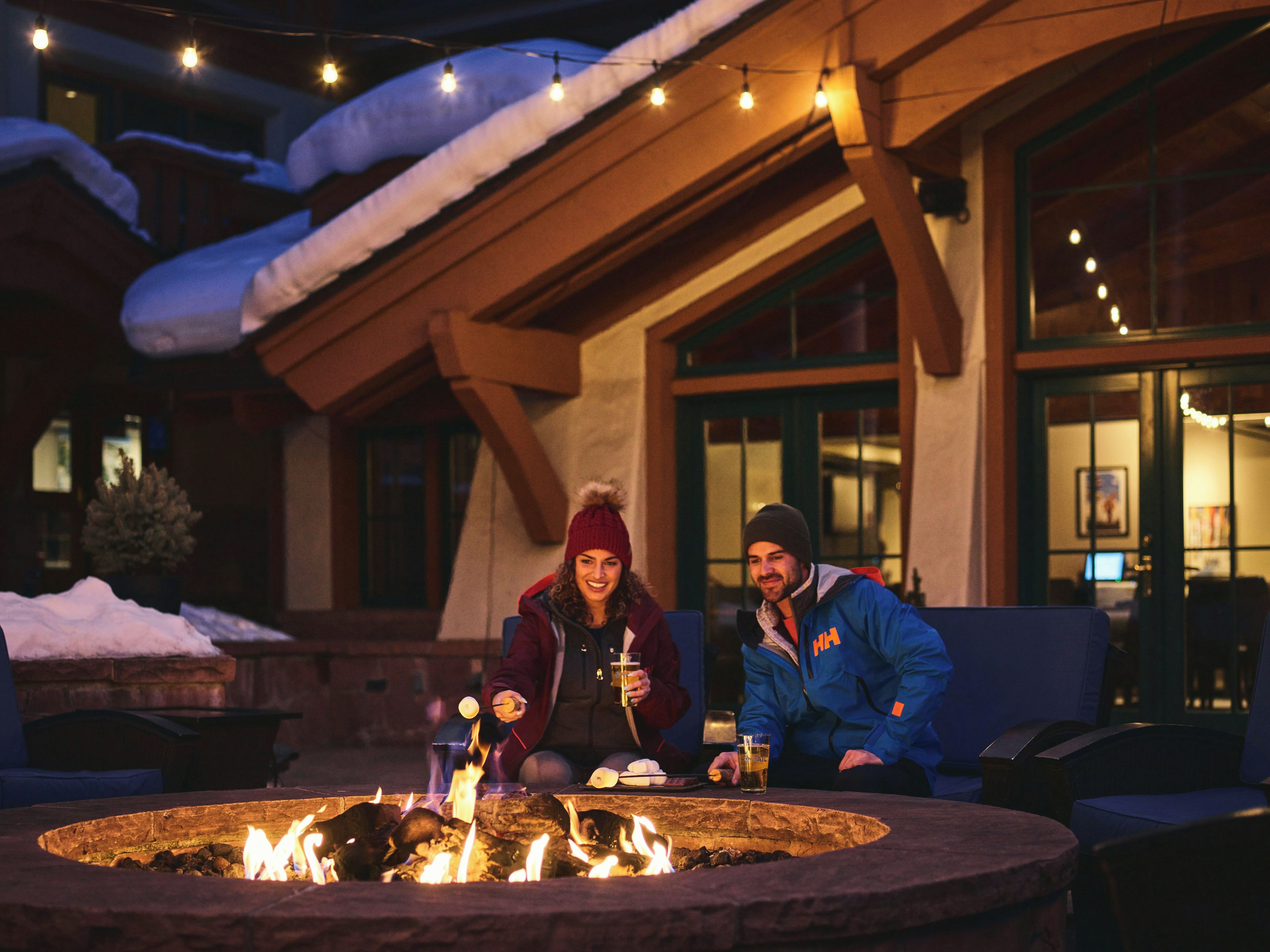A couple seated at an outdoor fire pit with a building in the background.