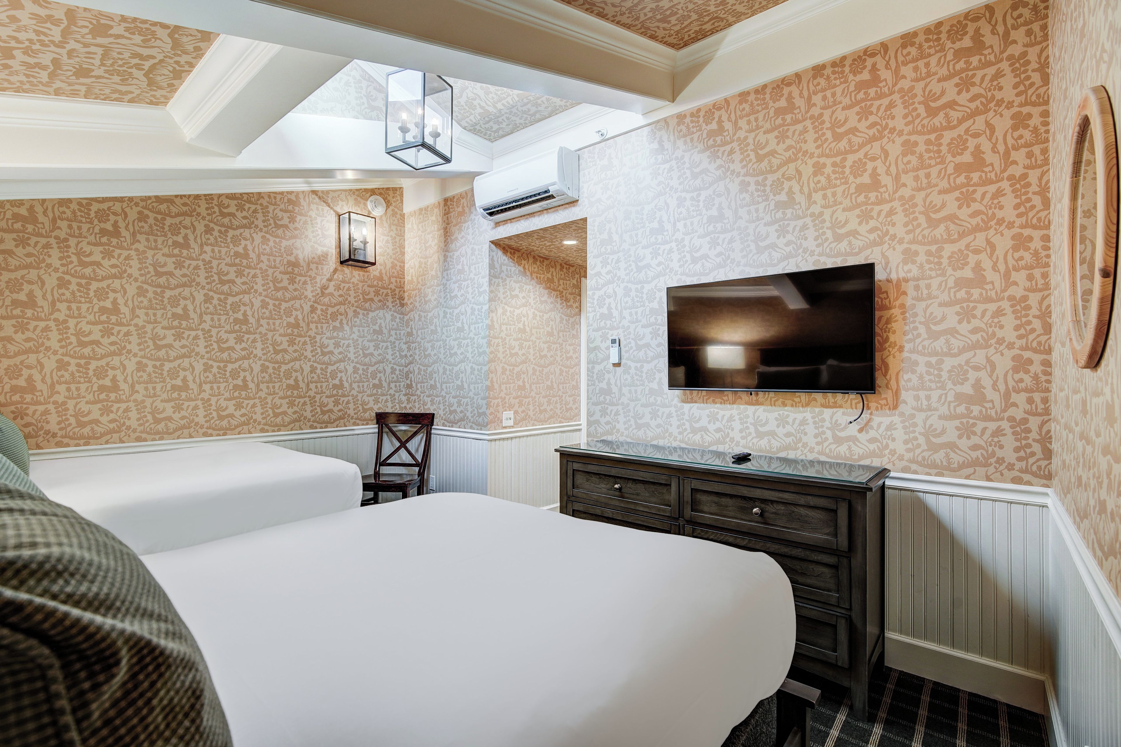 A hotel room with a large bed, a dresser, a television mounted on the wall, and patterned wallpaper.