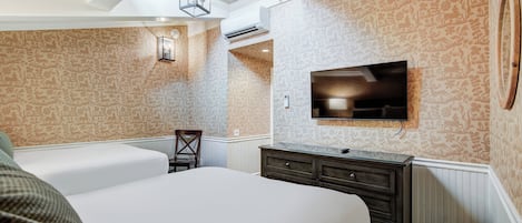A hotel room with a large bed, a dresser, a television mounted on the wall, and patterned wallpaper.
