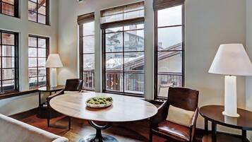 A room with a round table, two chairs, a bowl of snacks, and large windows with a view of buildings.