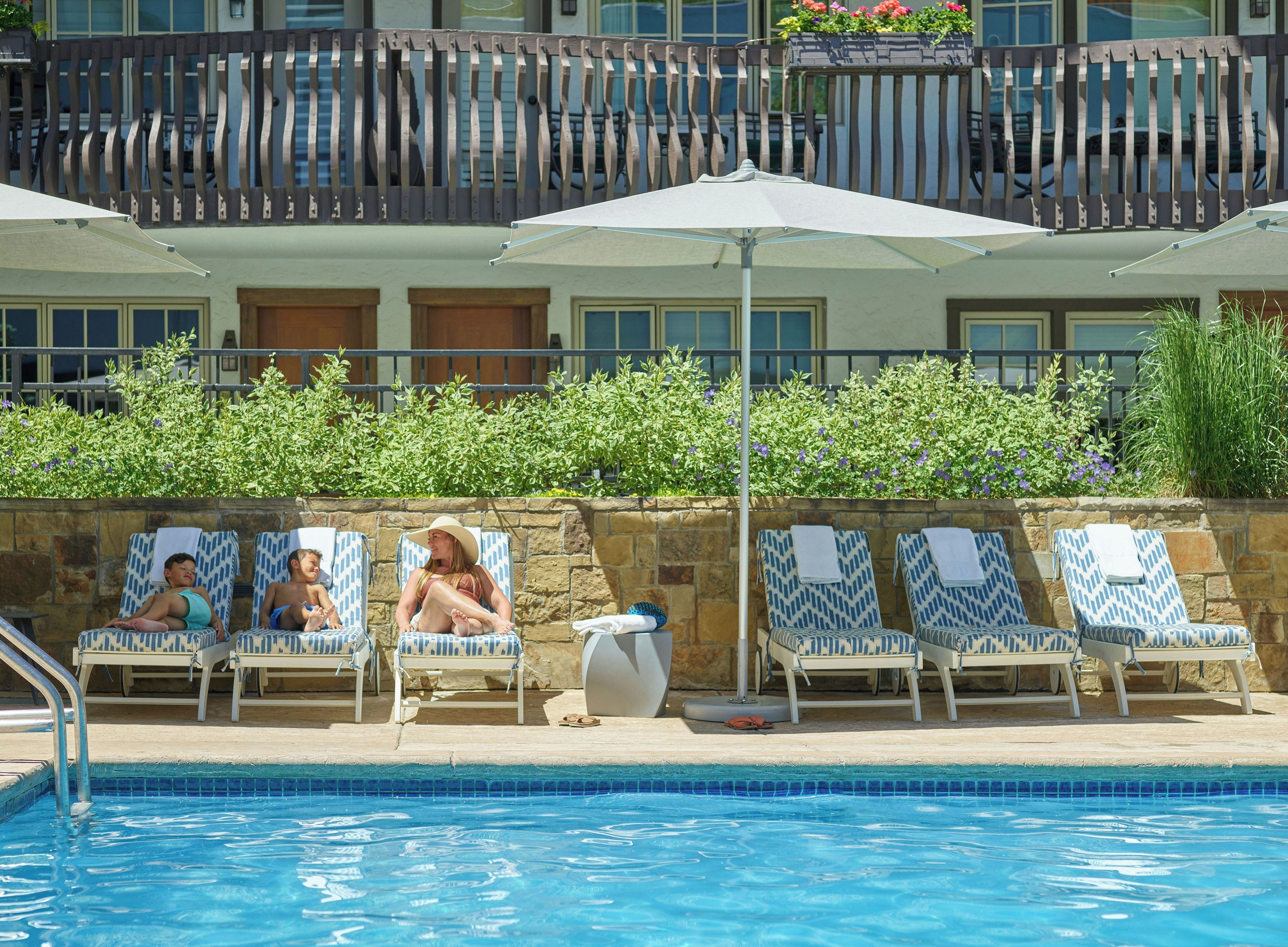 A poolside area with lounge chairs, a pool, and a building with a balcony.