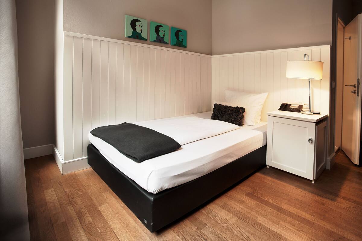 A neatly arranged bedroom with a bed, bedside table, and a wall-mounted artwork.