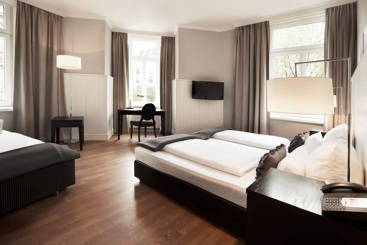 A hotel room with a bed, desk, chair, and a TV mounted on the wall.