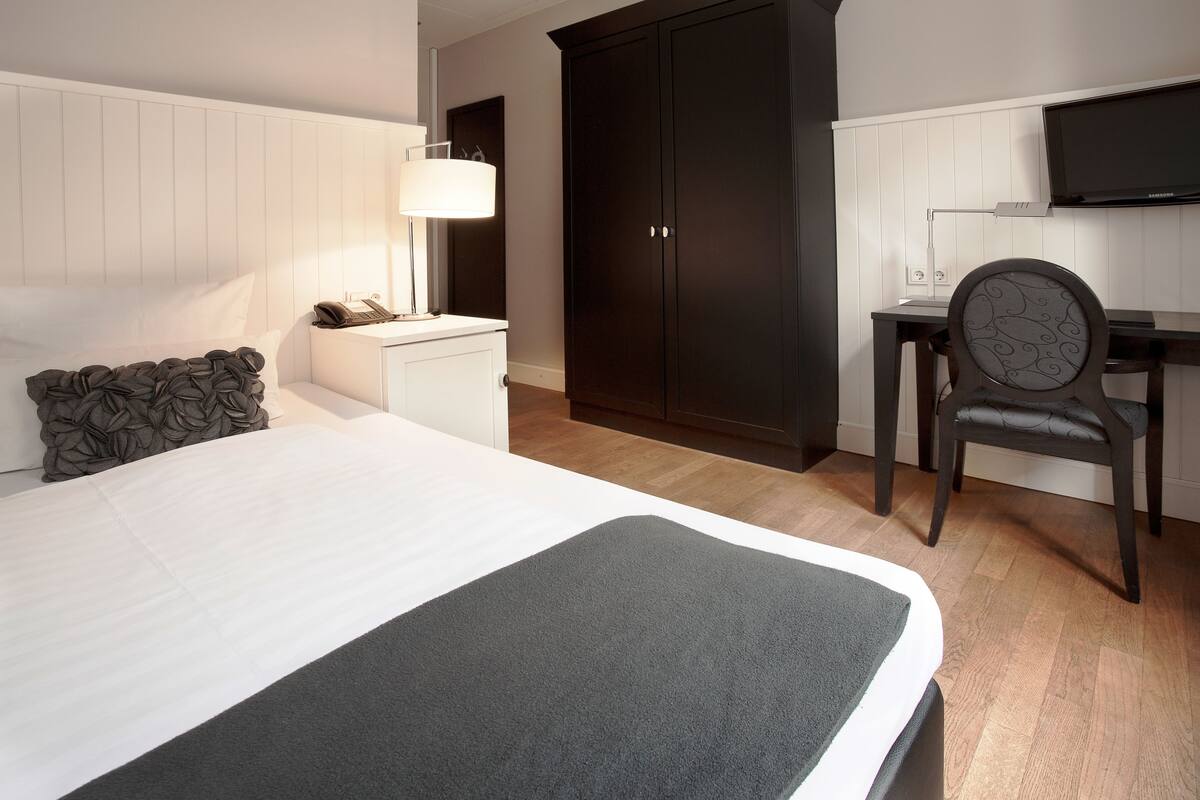 A hotel room with a bed, a desk, a chair, a wardrobe, and a television.
