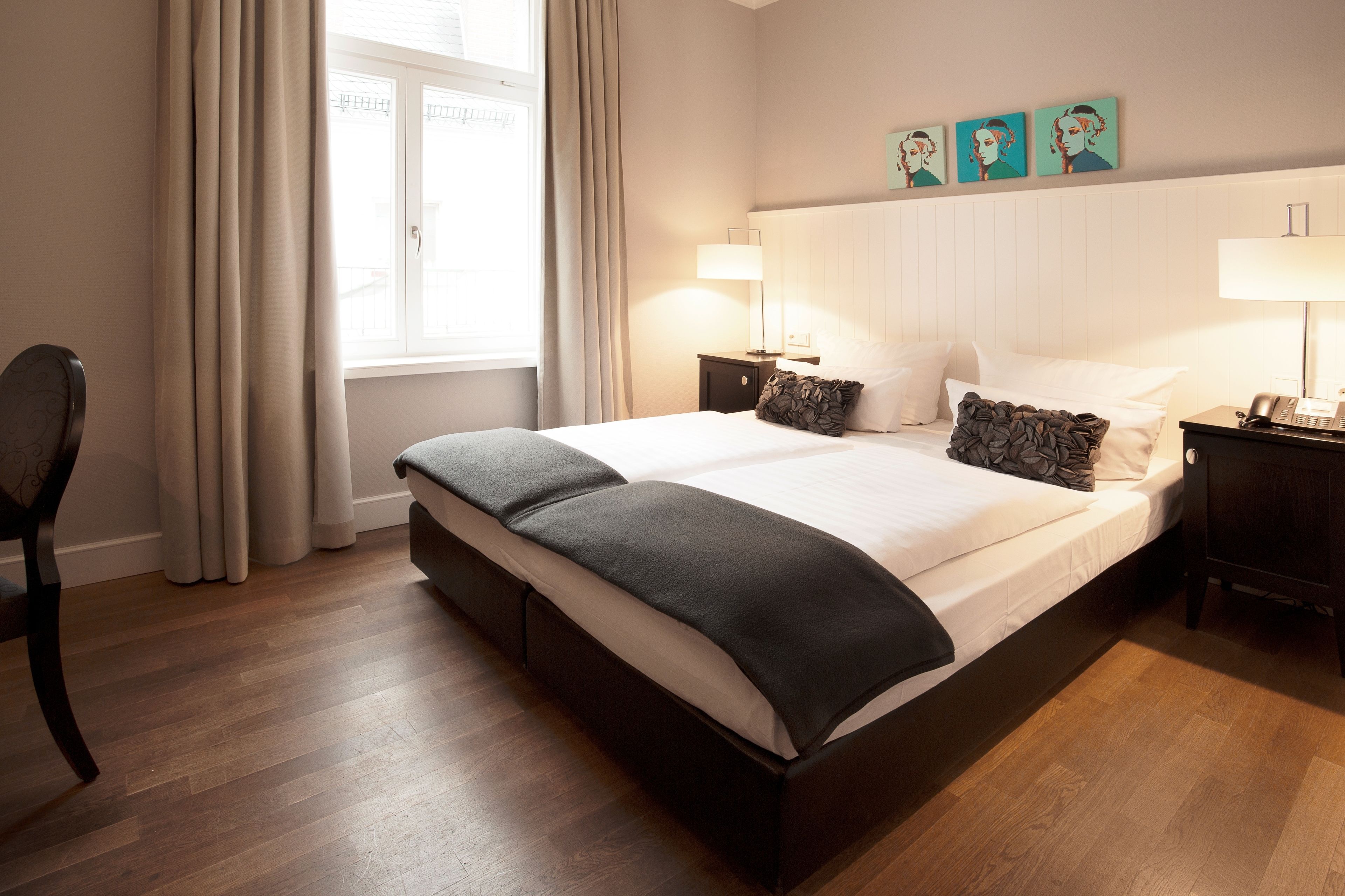 A hotel room with a large bed, two bedside tables, a chair, and a window with curtains.