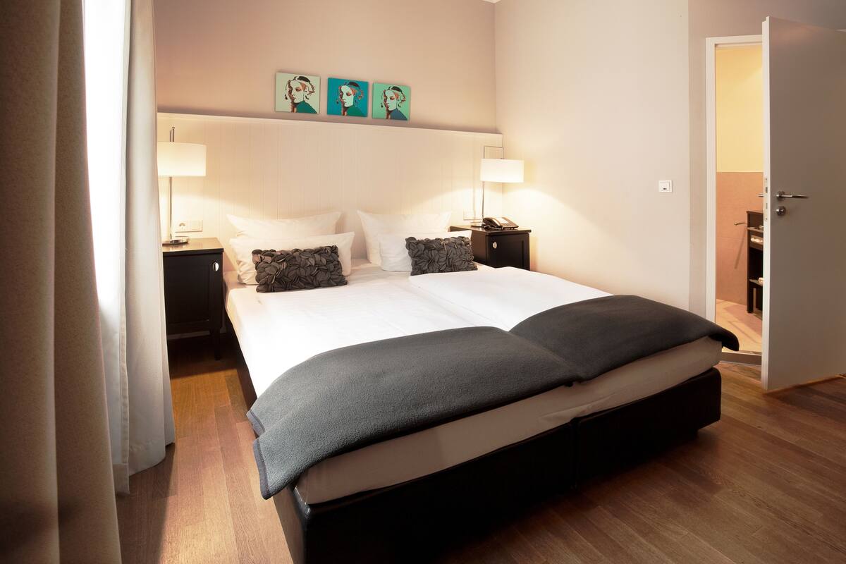 A neatly made bed with a dark headboard, two bedside tables with lamps, and a door leading to another room.