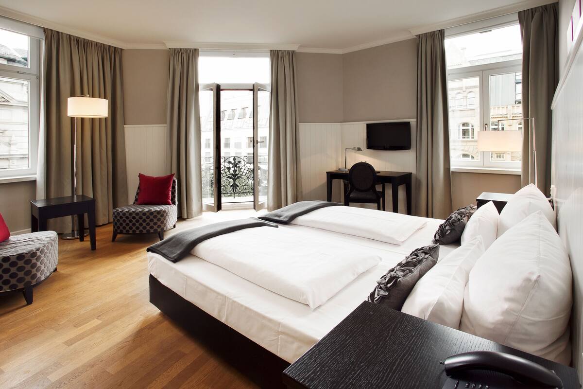 A hotel room with a large bed, a desk, a chair, and a TV.