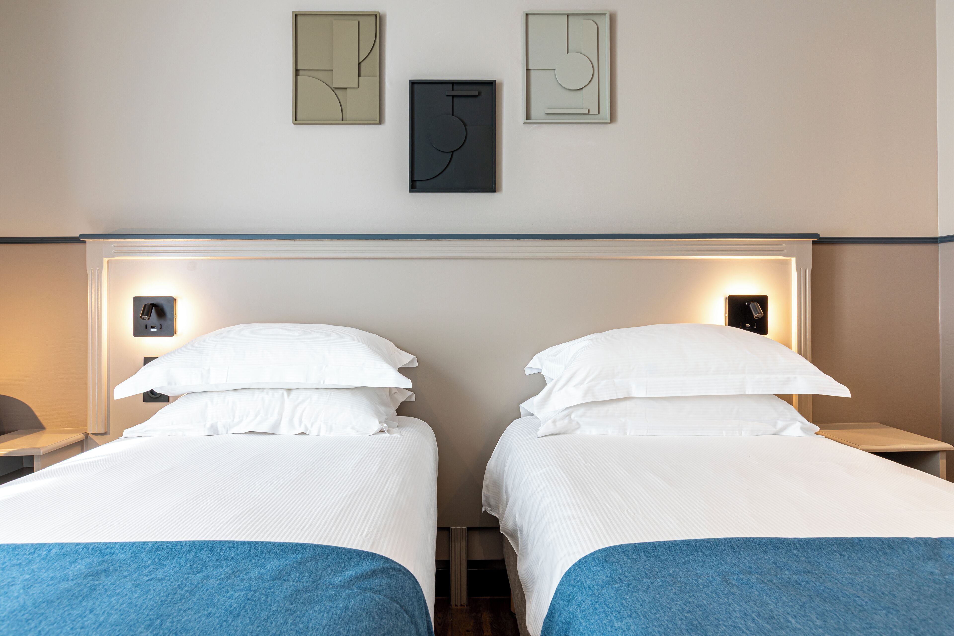 A hotel room with two beds, a headboard, wall-mounted artwork, and bedside lamps.