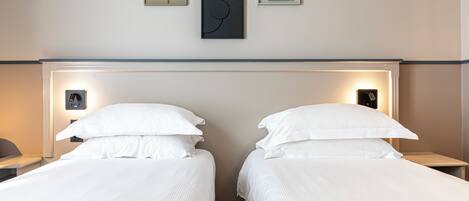 A hotel room with two beds, a headboard, wall-mounted artwork, and bedside lamps.