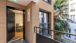 Una entrada moderna a un edificio con una puerta marcada '3', un pequeño espacio de descanso en el interior y un balcón con barandilla.