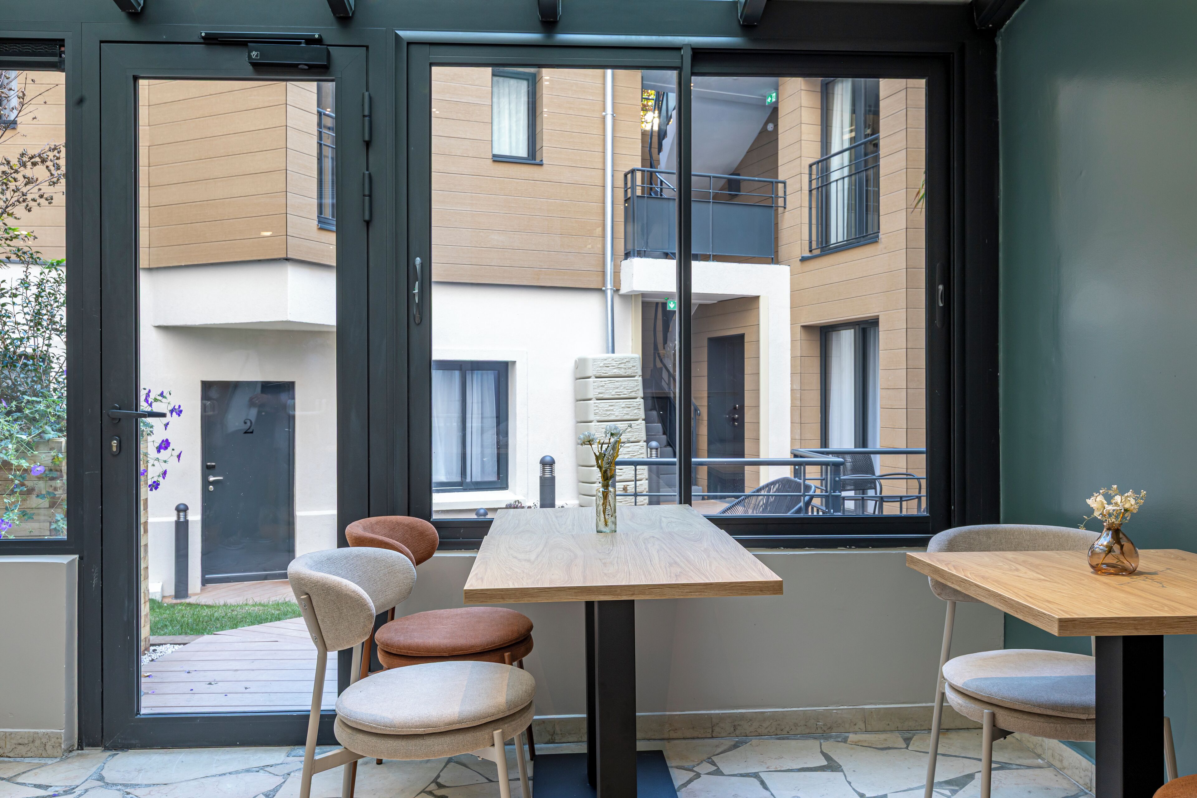 A modern interior with a wooden table and chairs, a vase with flowers, and a view of a building with balconies.