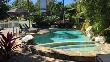 A pool area with lounge chairs, umbrellas, and tropical plants.